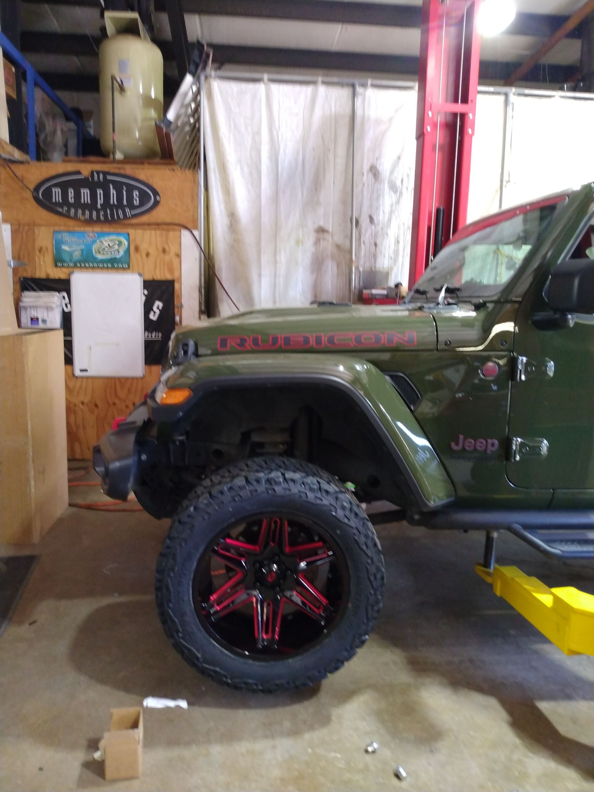 A green jeep is on a lift in a garage