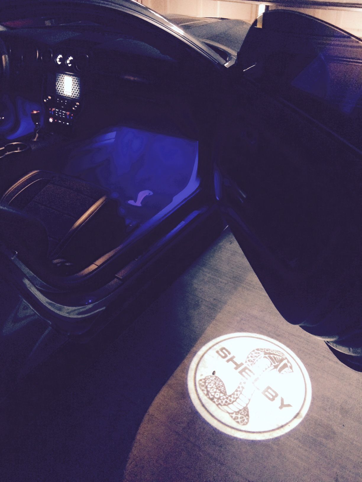 A shelby logo is projected onto the floor of a car