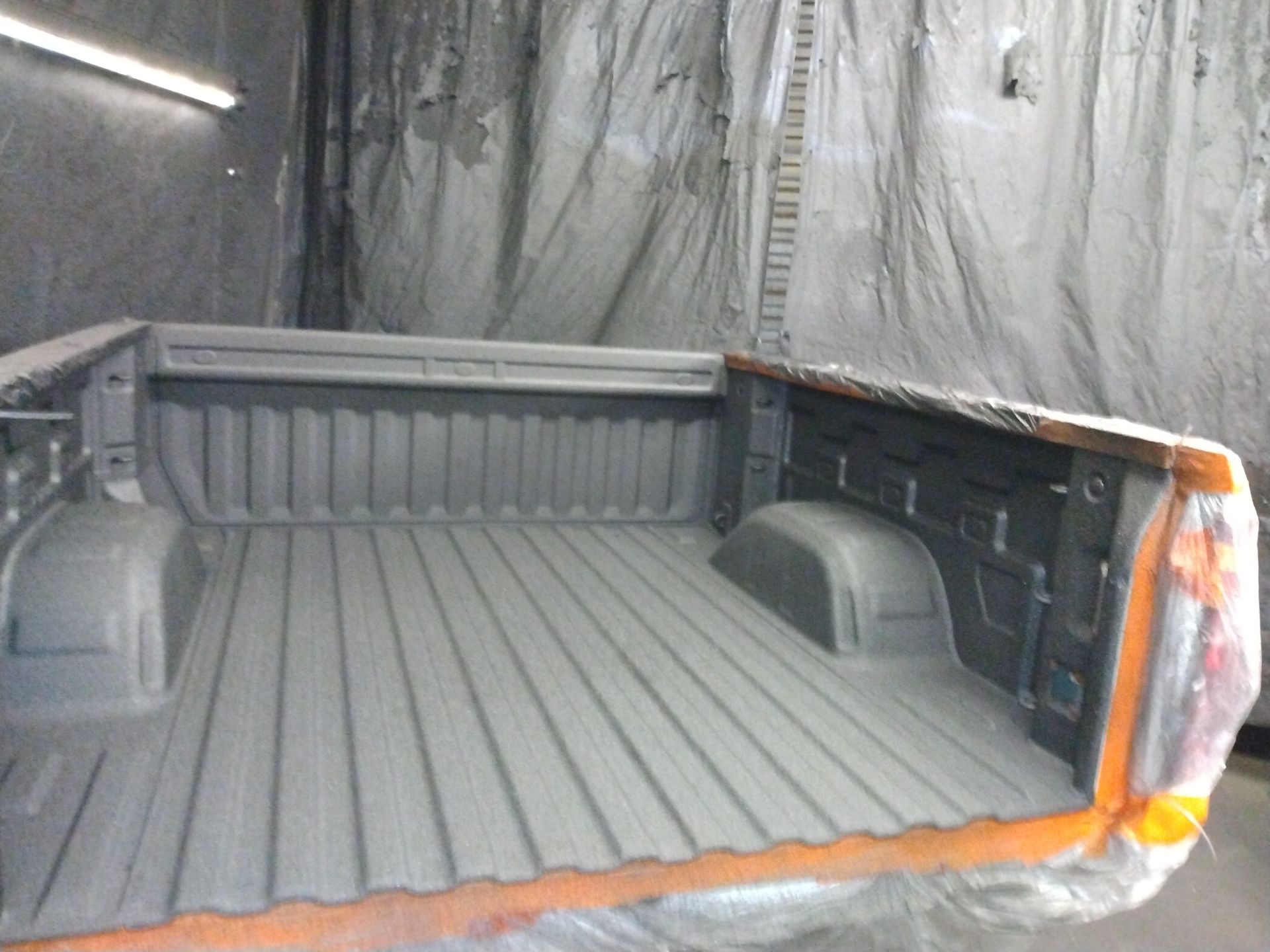A truck bed is being painted in a paint booth
