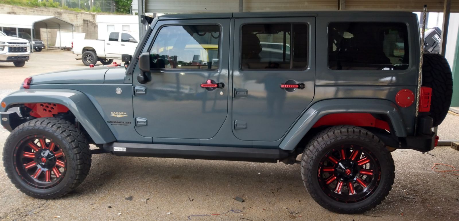 A gray jeep with red fender flares and black wheels is parked in a parking lot.