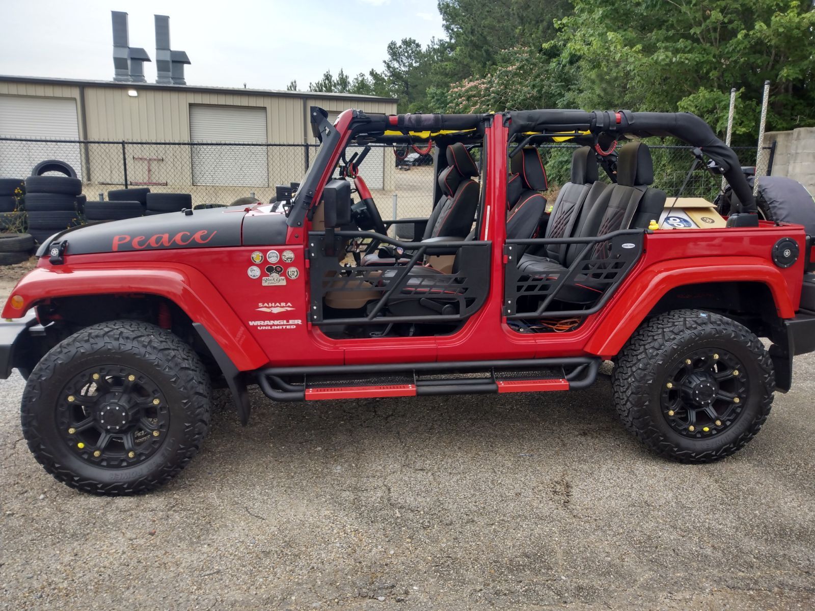 A red jeep with the doors open is parked in a parking lot.