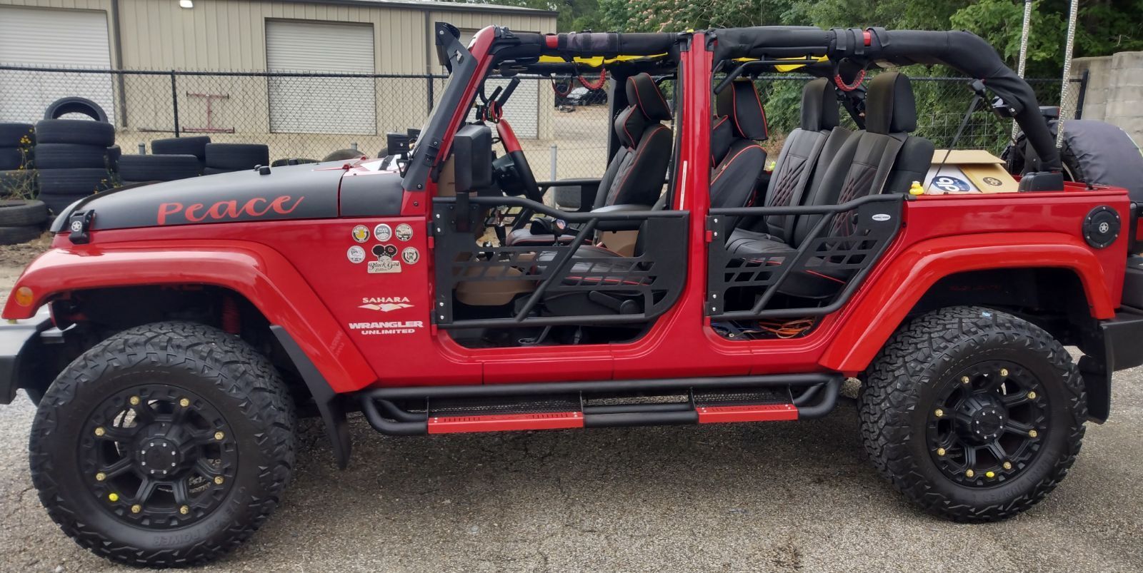 A red jeep with the doors open is parked in a gravel lot.