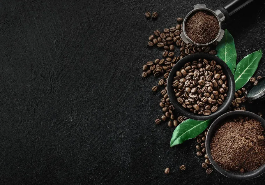 Three bowls of coffee beans and ground coffee on a black background.