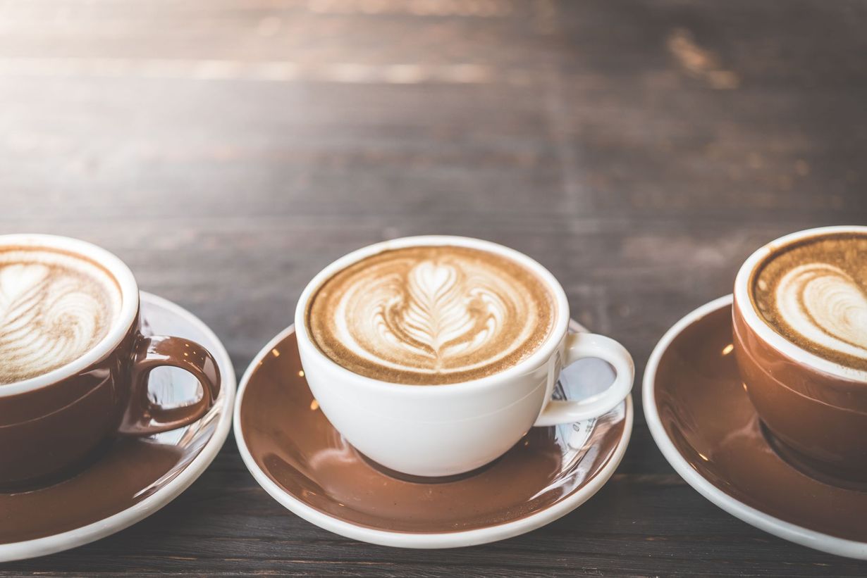 Three cups of coffee are sitting on saucers on a wooden table.