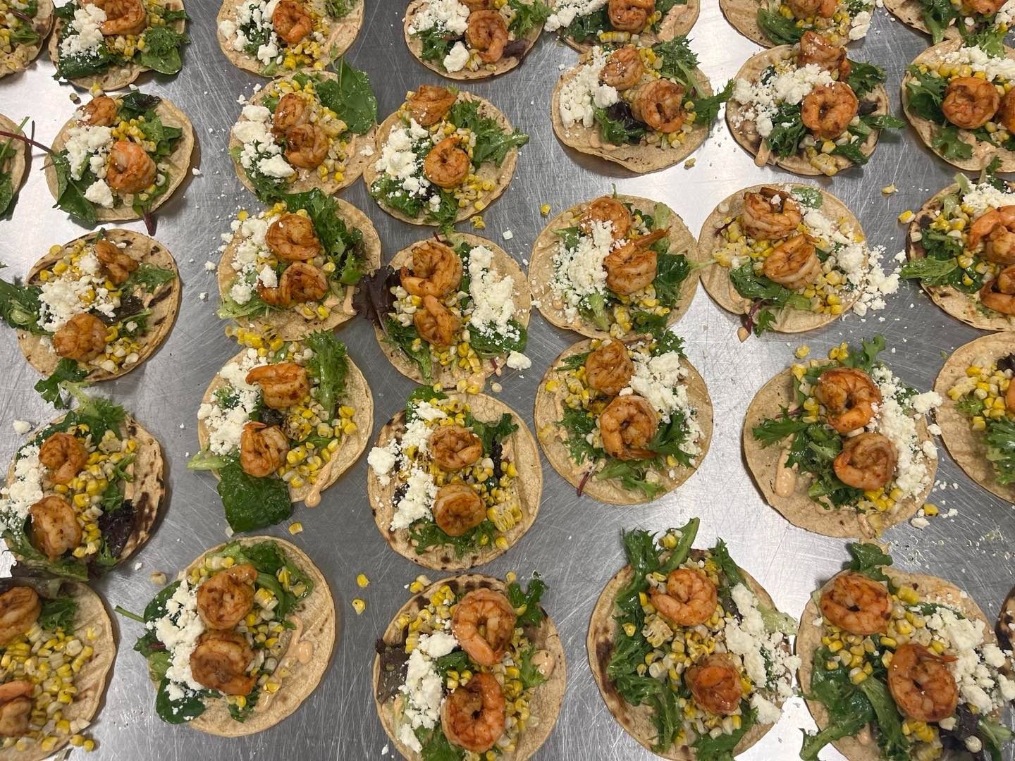 Miniature shrimp tacos on a tray, topped with greens, cheese, and corn.