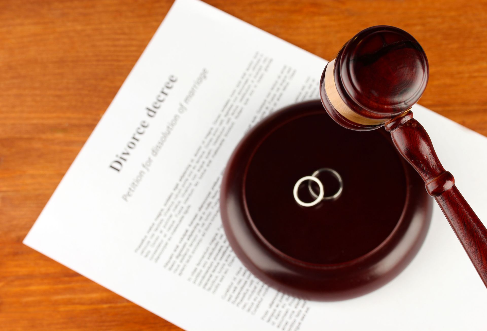 Two wedding rings are sitting next to a gavel and a divorce decree.