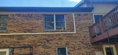 The back of a brick house with a balcony and a lot of windows.