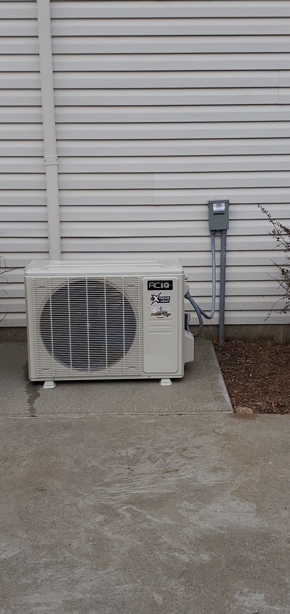 A white air conditioner is sitting on the sidewalk in front of a white house.