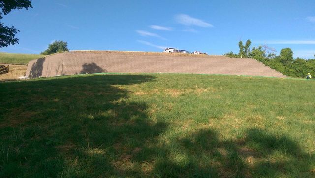 A large hill in the middle of a grassy field with a blue sky in the background.