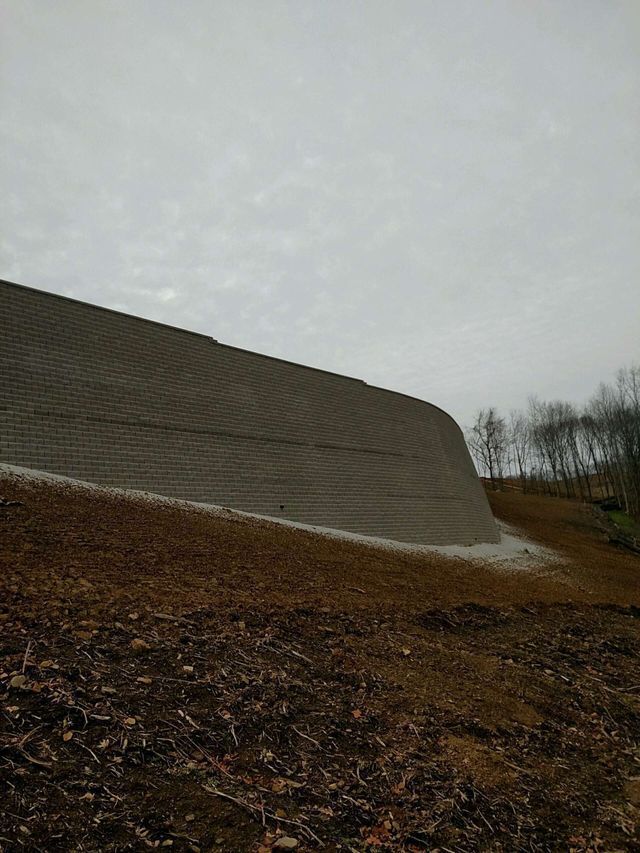 A large concrete wall is sitting on top of a dirt hill.