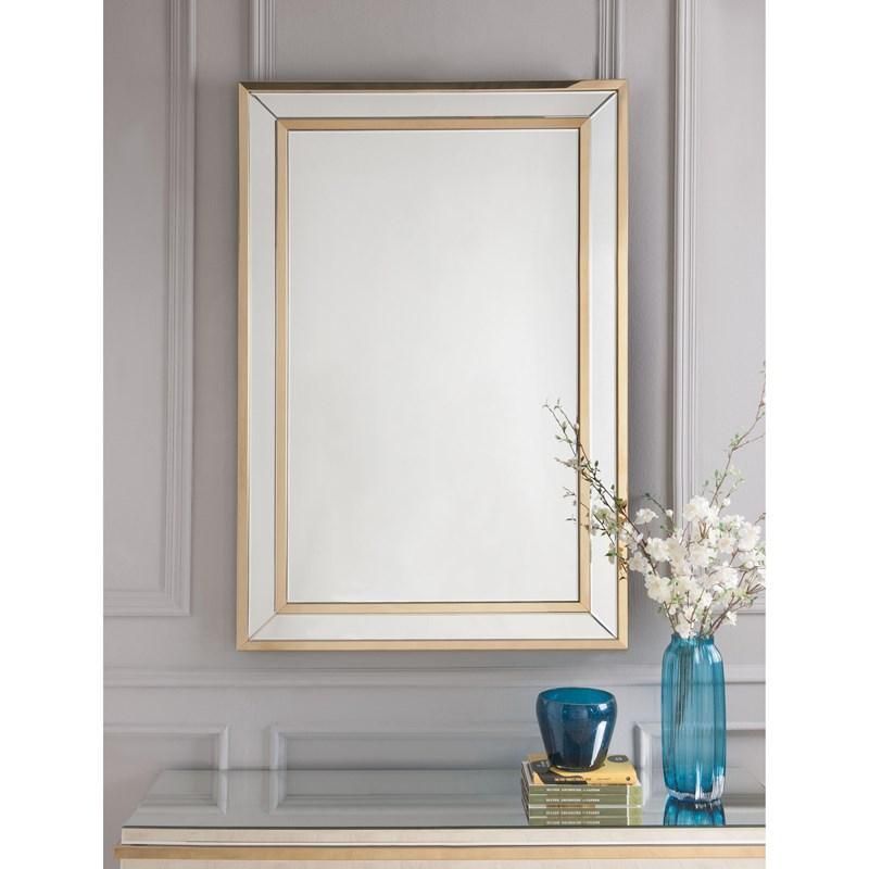 A mirror with a gold frame is hanging on a wall next to a vase of flowers.