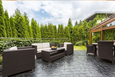 A patio with wicker furniture and a table in the middle of a forest.