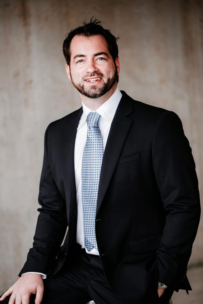 A man in a suit and tie is sitting with his hands in his pockets.