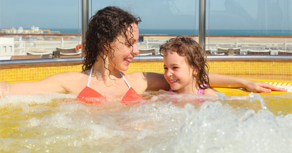 Woman and child in a bubbly hot tub, smiling at each other. They are on a cruise ship deck.