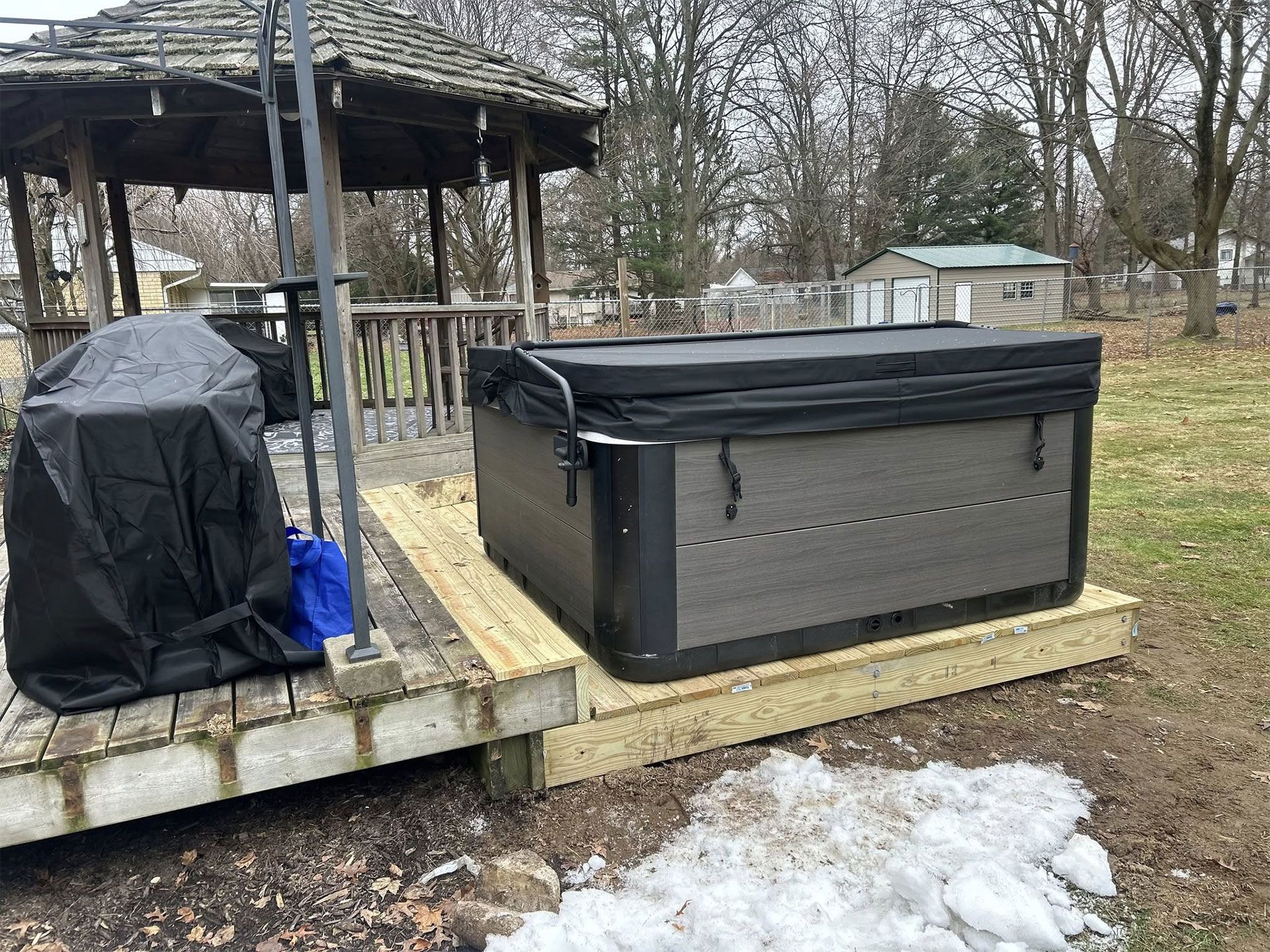 A hot tub is sitting on top of a wooden deck next to a gazebo.
