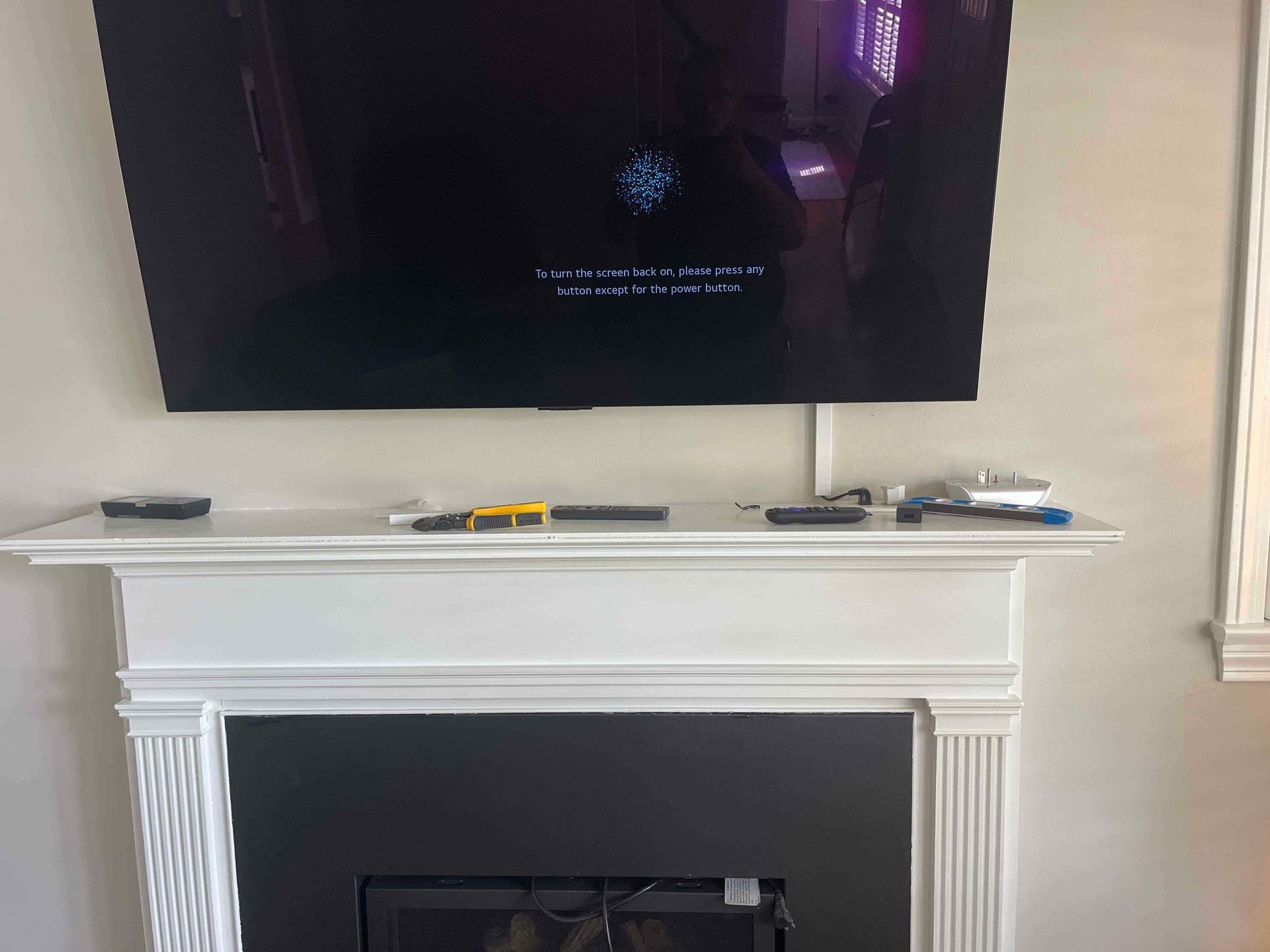 Large TV mounted above a white fireplace mantel. Tools and remote rest on the mantel.