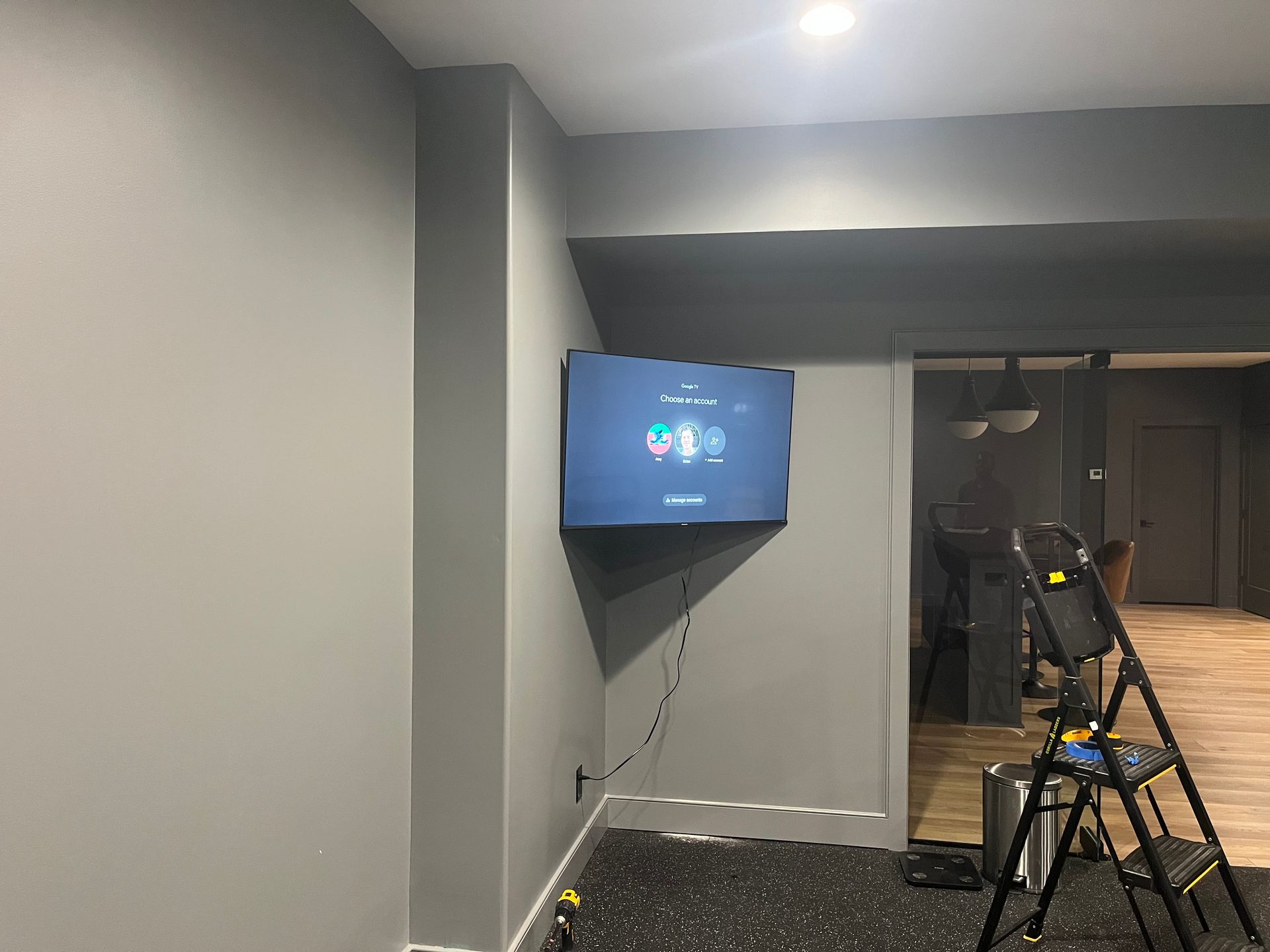 Gray walls with a mounted TV in the corner; a ladder and tools are present.