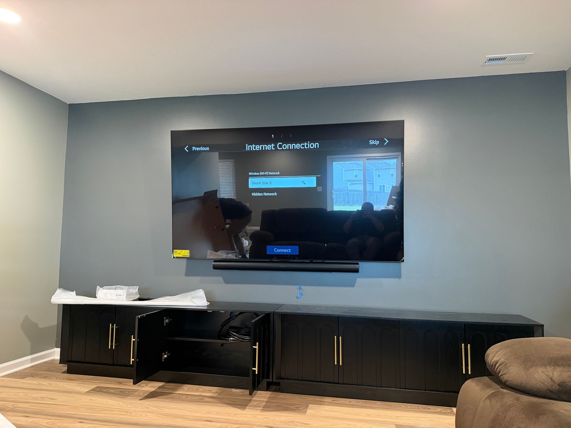 Large TV mounted on a blue wall with a black entertainment center below; the TV displays an internet connection screen. 