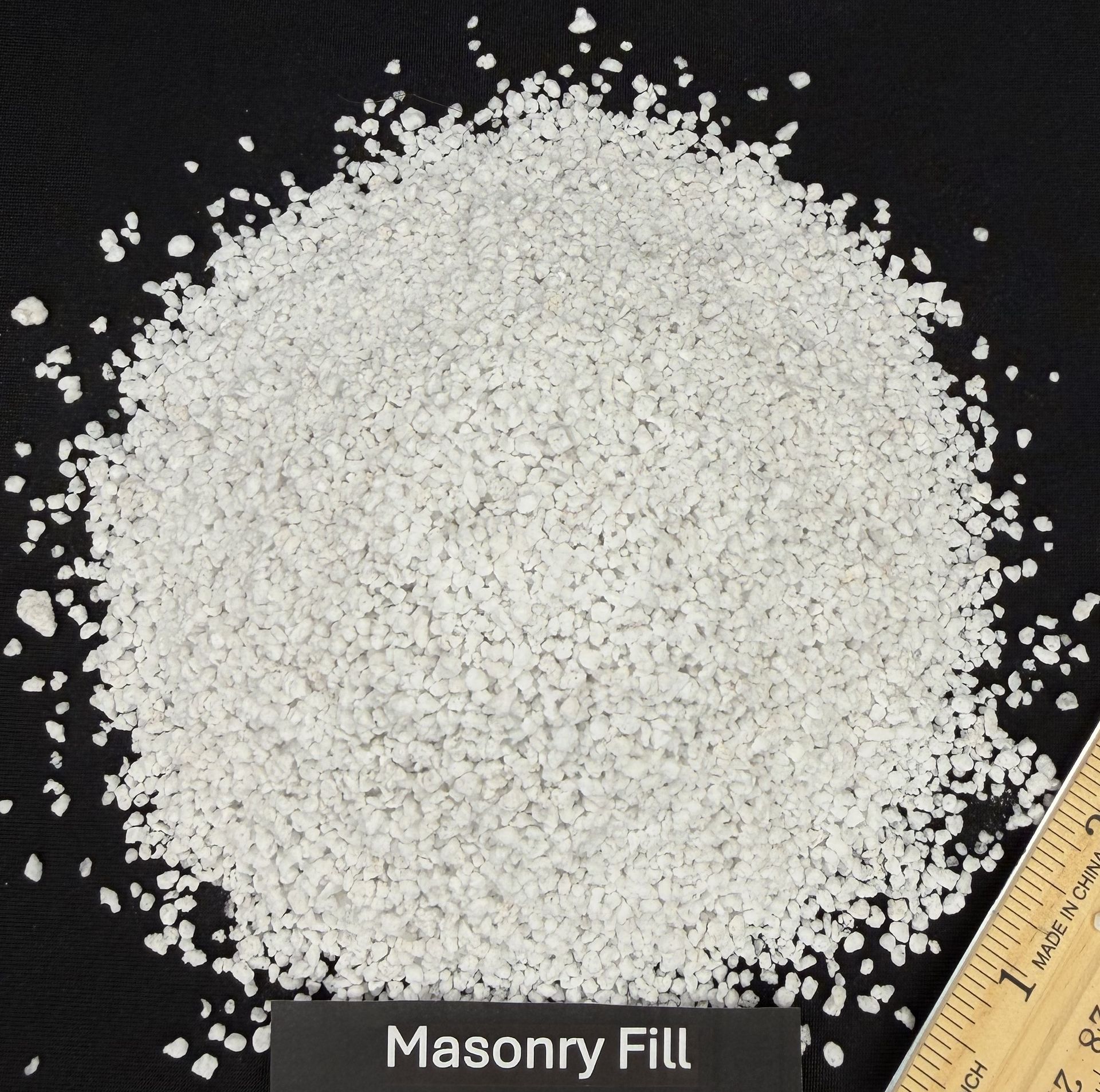 White masony fill gravel pile on a black background with a ruler at the edge