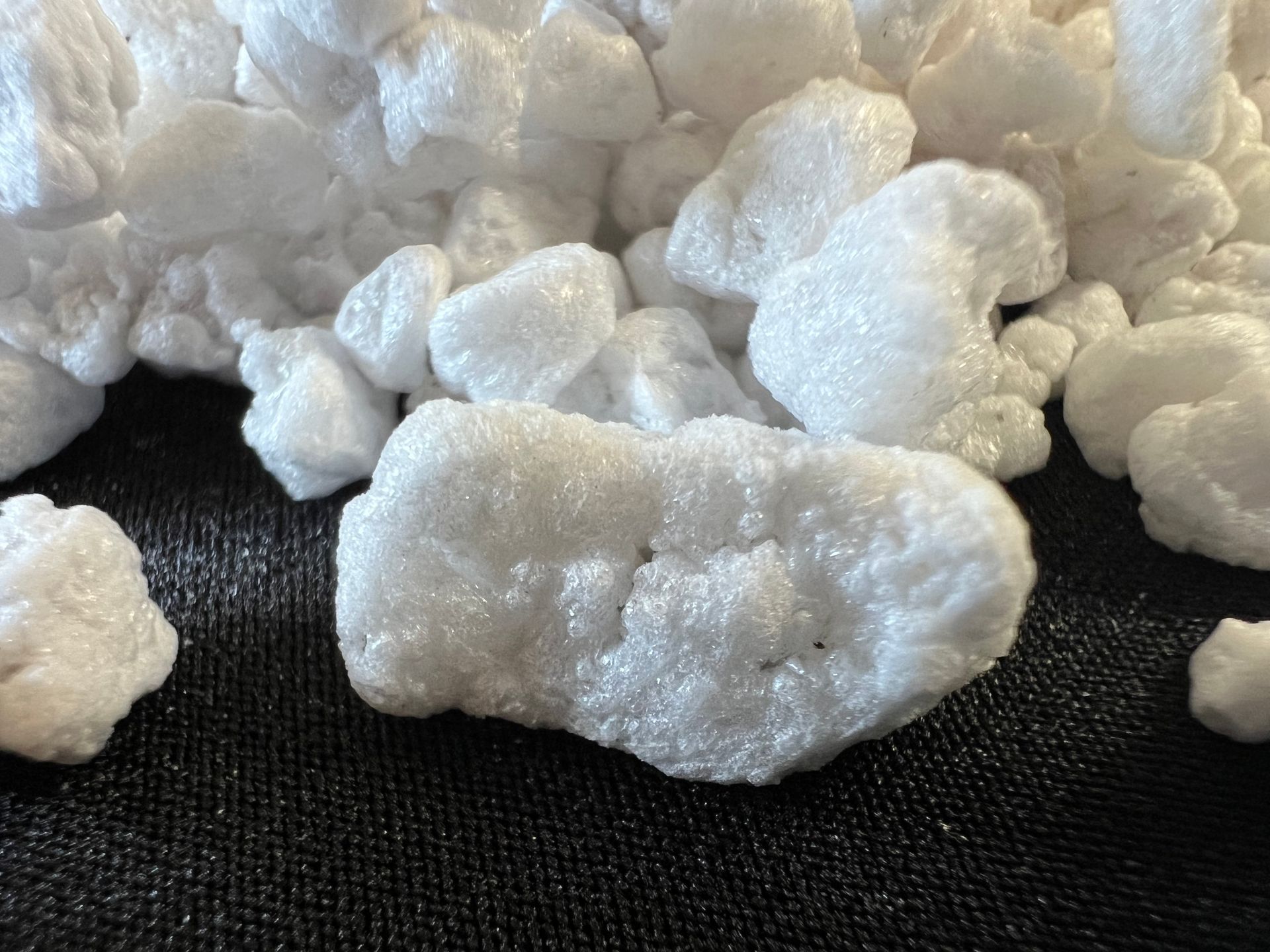 White, fluffy mineral-like crystals scattered on a dark surface