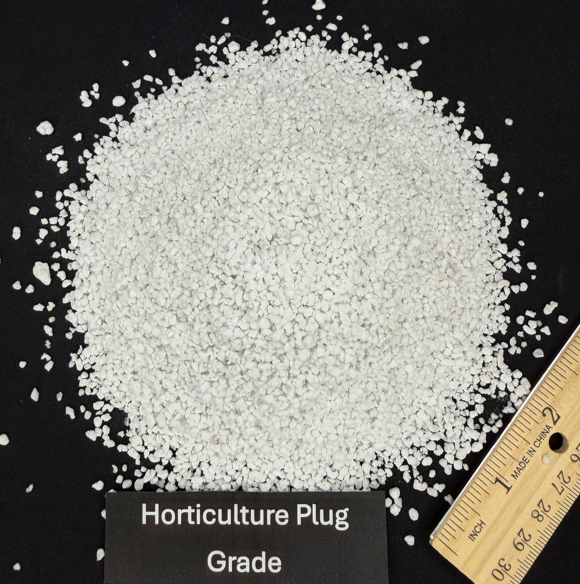 Pile of white horticulture plug grade pellets on a black background with a ruler for scale