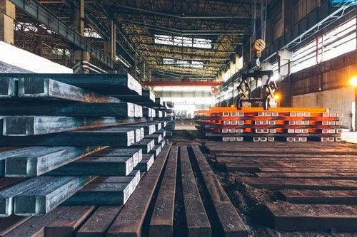 Industrial warehouse with stacked steel beams, rails, and orange metal racks under a high roof
