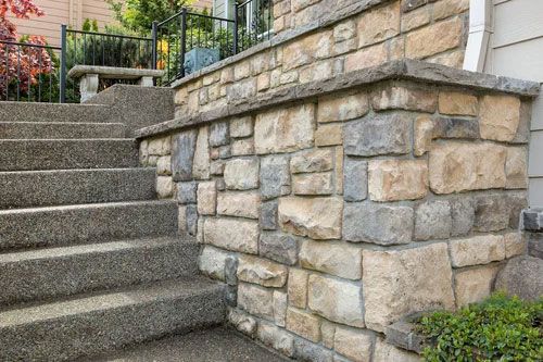 Stone retaining wall beside concrete steps in a landscaped outdoor area