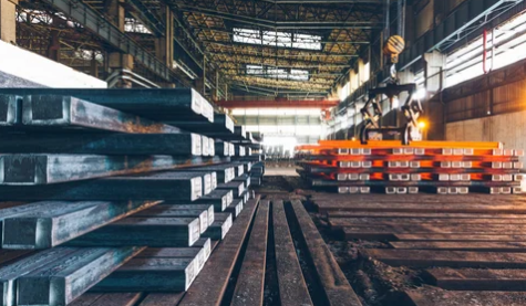 Steel beams stacked in an industrial warehouse with orange racks and tracks on the floor