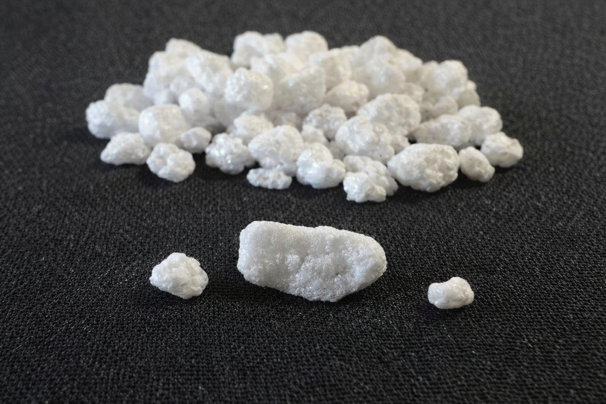 White crystalline granules on a dark surface, with one larger piece in front.