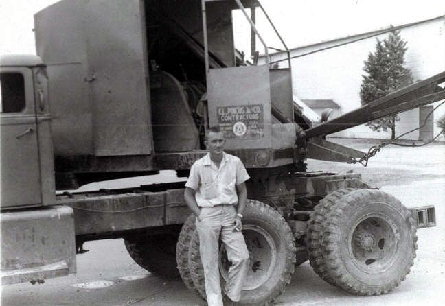 A black and white photo of a man standing next to a truck