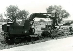 A black and white photo of an excavator digging a hole in a field.