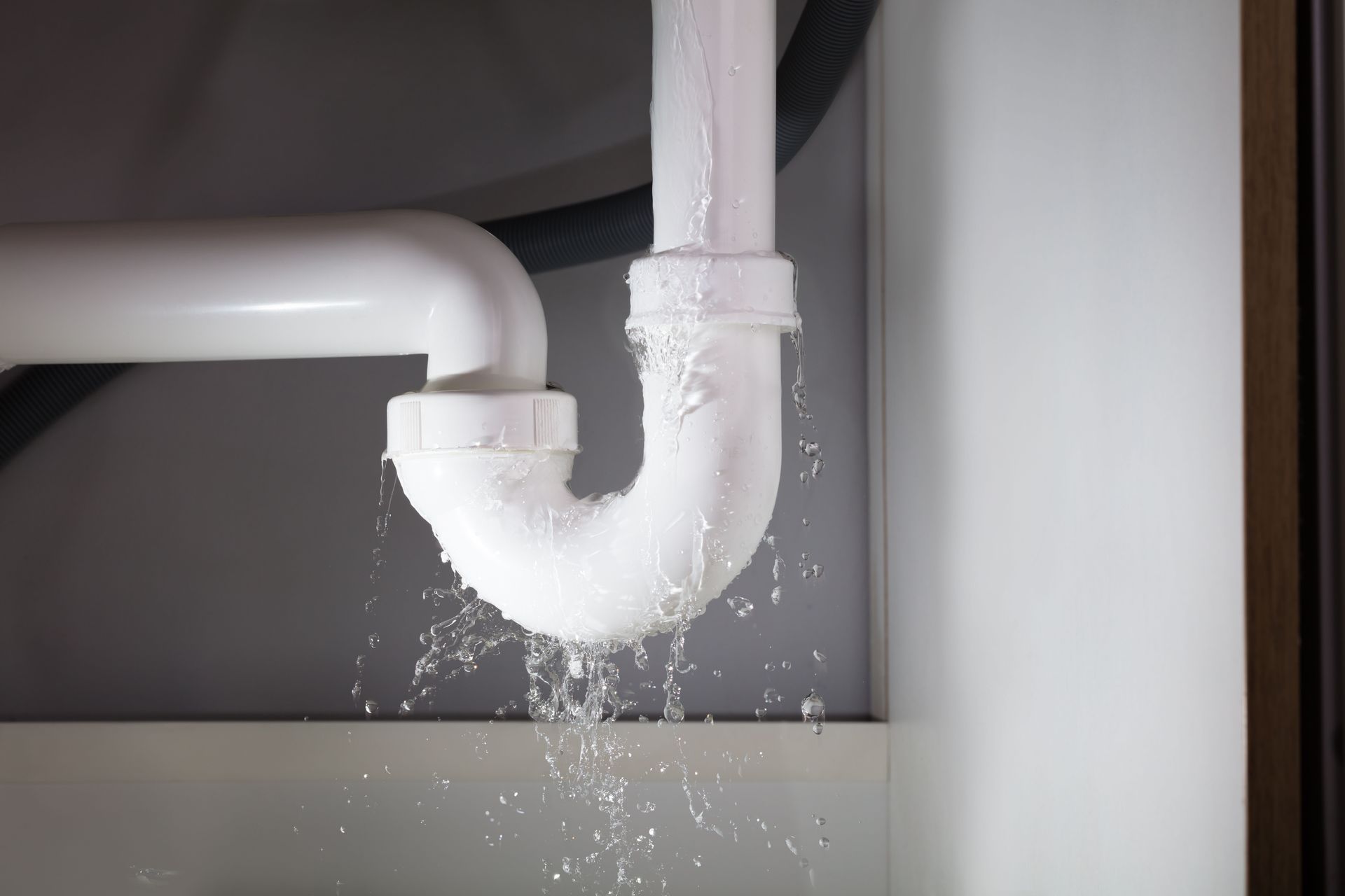 Leaking white pipe under a sink, water dripping into a basin