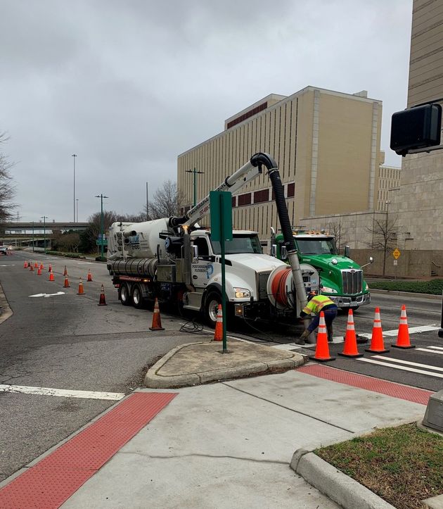 Utility truck and cone-marked sidewalk repair beside a building on a wet city street