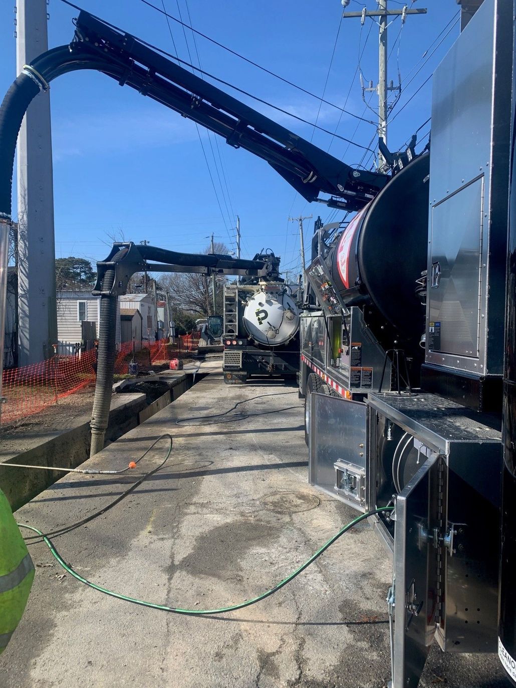 Industrial machinery with large blue hoses and tanks along a concrete yard under a clear sky