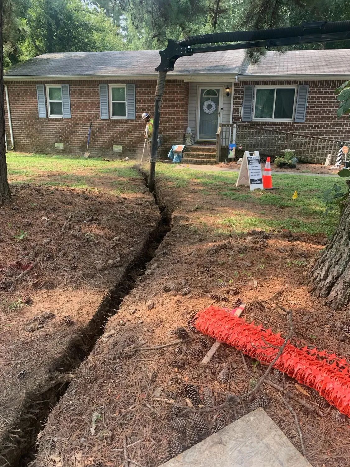 Cracked yard with a deep trench leading to a brick house and fallen tree debris near the driveway