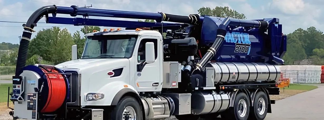 White tanker truck with blue hose equipment parked outdoors on a roadside