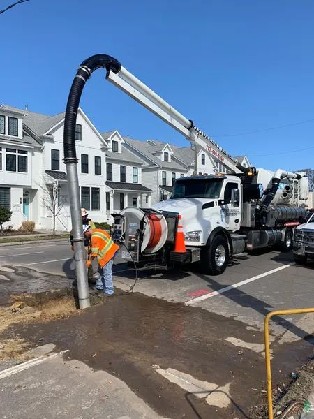 Worker clearing street debris with a vacuum truck in front of townhouses