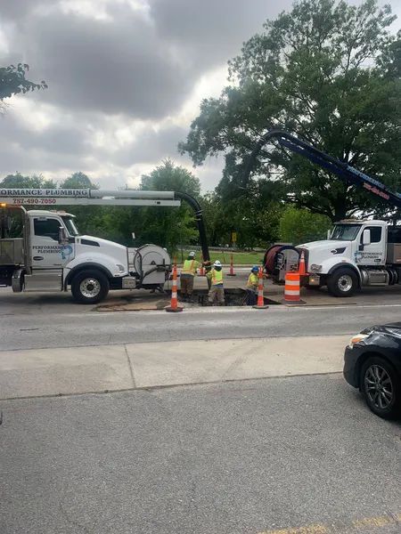 Utility workers and trucks repairing road drainage near orange cones under cloudy skies