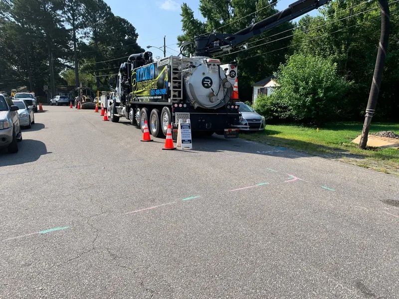 Utility truck with equipment and orange cones blocking a tree-lined residential street during maintenance.