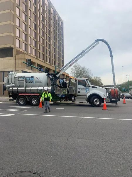 Concrete pump truck and workers on a street beside a tall building, with the pump boom arched overhead.