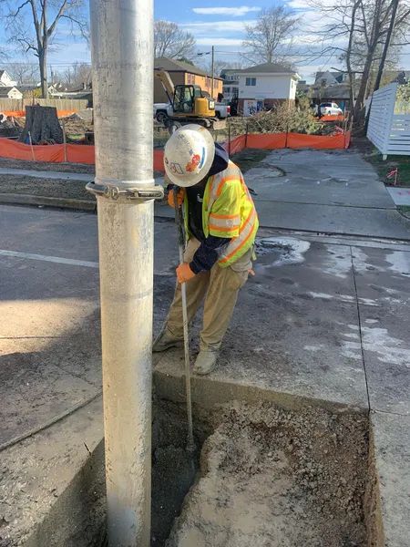 Construction worker in safety vest digging around a utility pole on a sidewalk