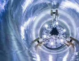Inside a futuristic blue tunnel, a circular mechanical device glows with bright lights at the center.