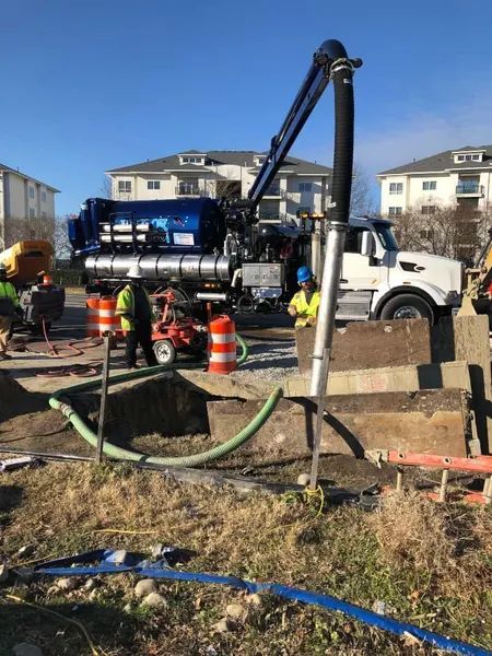 Utility truck with vacuum hose and crew working on a roadside excavation site