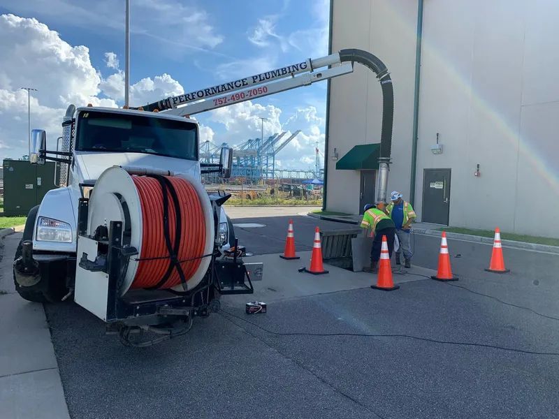 Utility truck with hose reel and workers cleaning beside a large white building under a boom arm