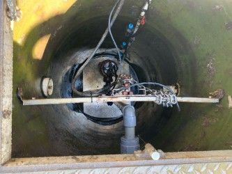 Inside a round tank, a pump, pipes, and cables are visible in a dirty industrial chamber.