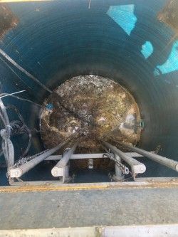Inside a large circular pipe, two metal pipes lead toward a debris-filled opening.