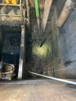 Abandoned mine tunnel with timber supports, mesh fence, and muddy floor lit by dim light