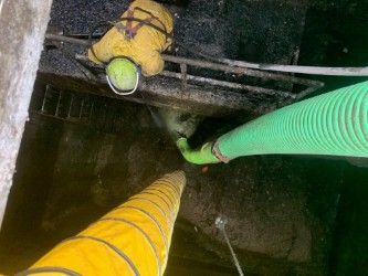Two large corrugated hoses, yellow and green, extending into a dark manhole or shaft