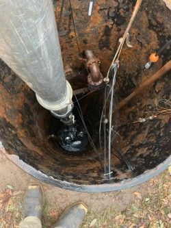View down a rusted well with a metal pipe, ropes, and muddy water inside.