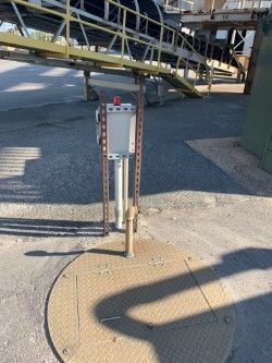 Metal electrical box and poles on a concrete pad beside industrial equipment outdoors